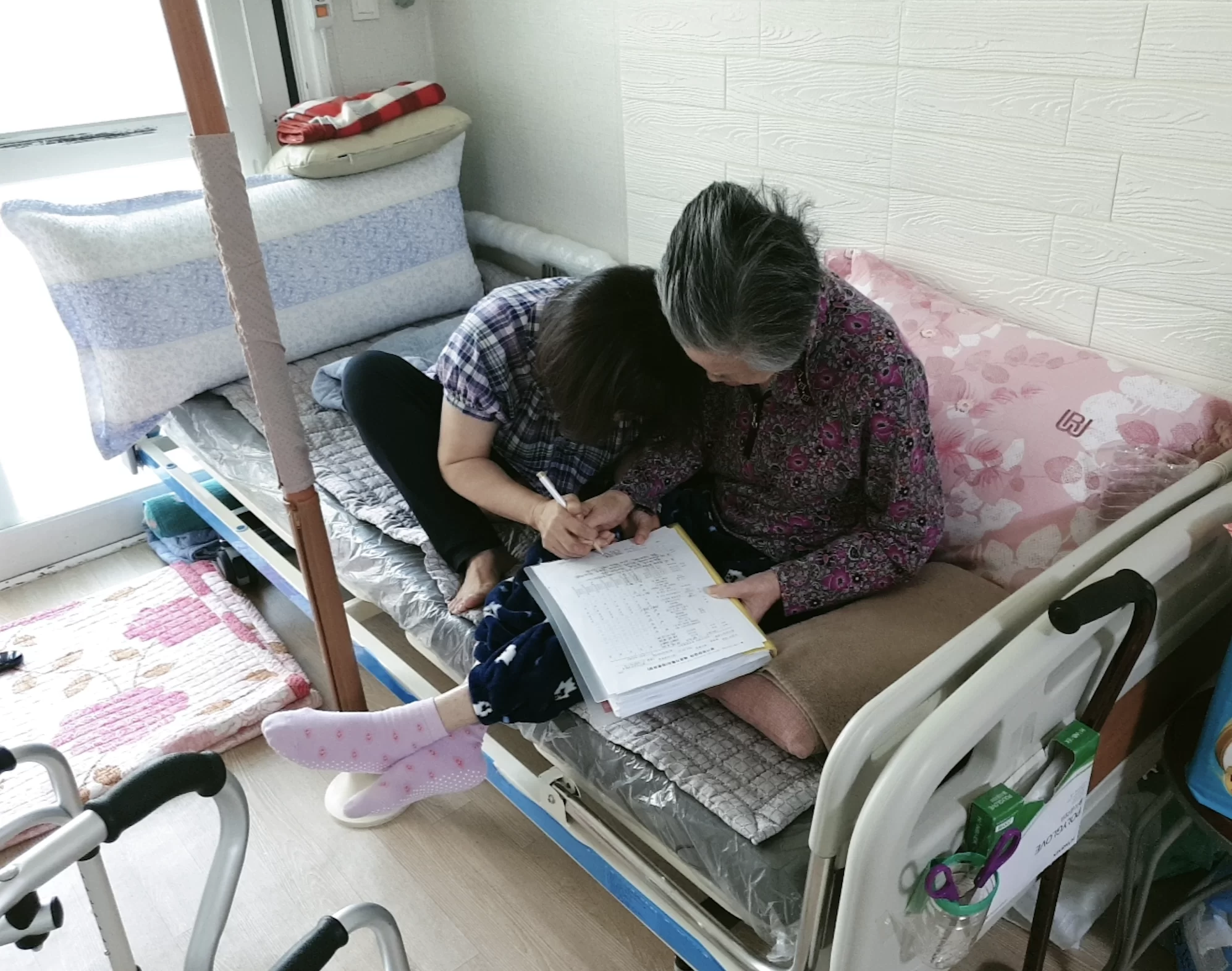 어르신이 침대에서 의사소견서 발급의뢰서를 확인하는 모습