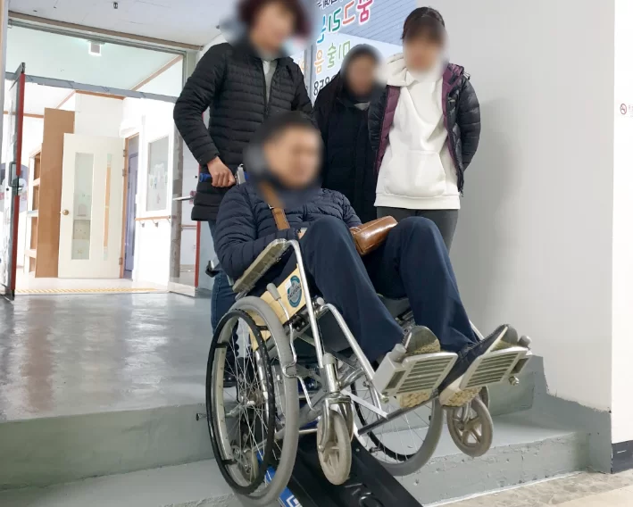 휠체어 이용 어르신과 보호자 모습을 통해 거동 불편·인지 불편 등 등급 신청 대상자 상태를 보여주는 케어링 이미지