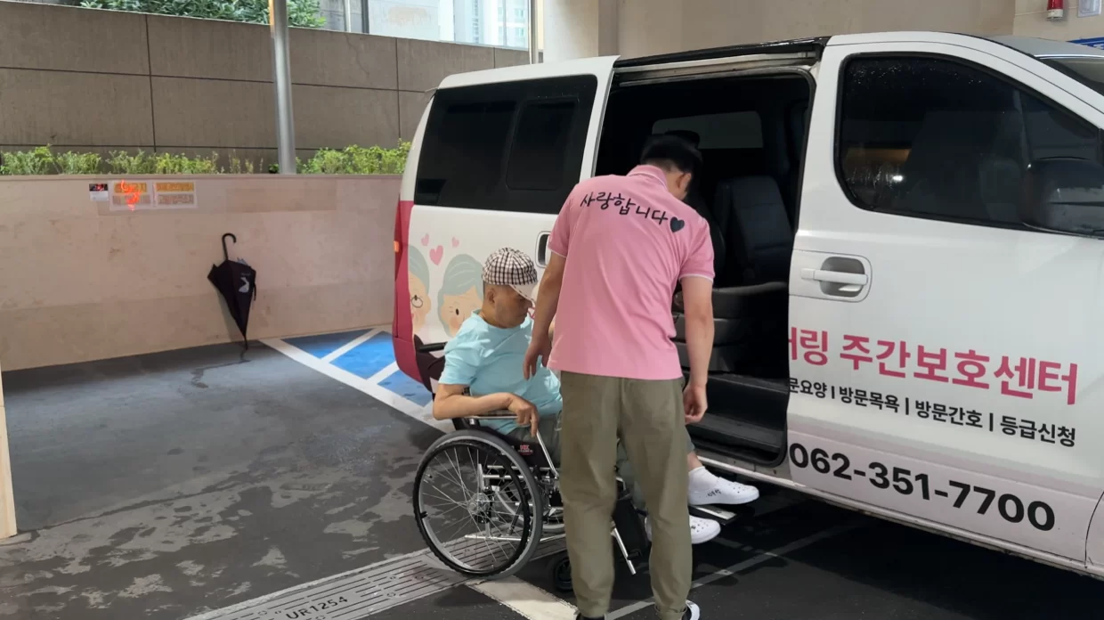 요양보호사가 휠체어 어르신 차량 탑승을 돕는 모습