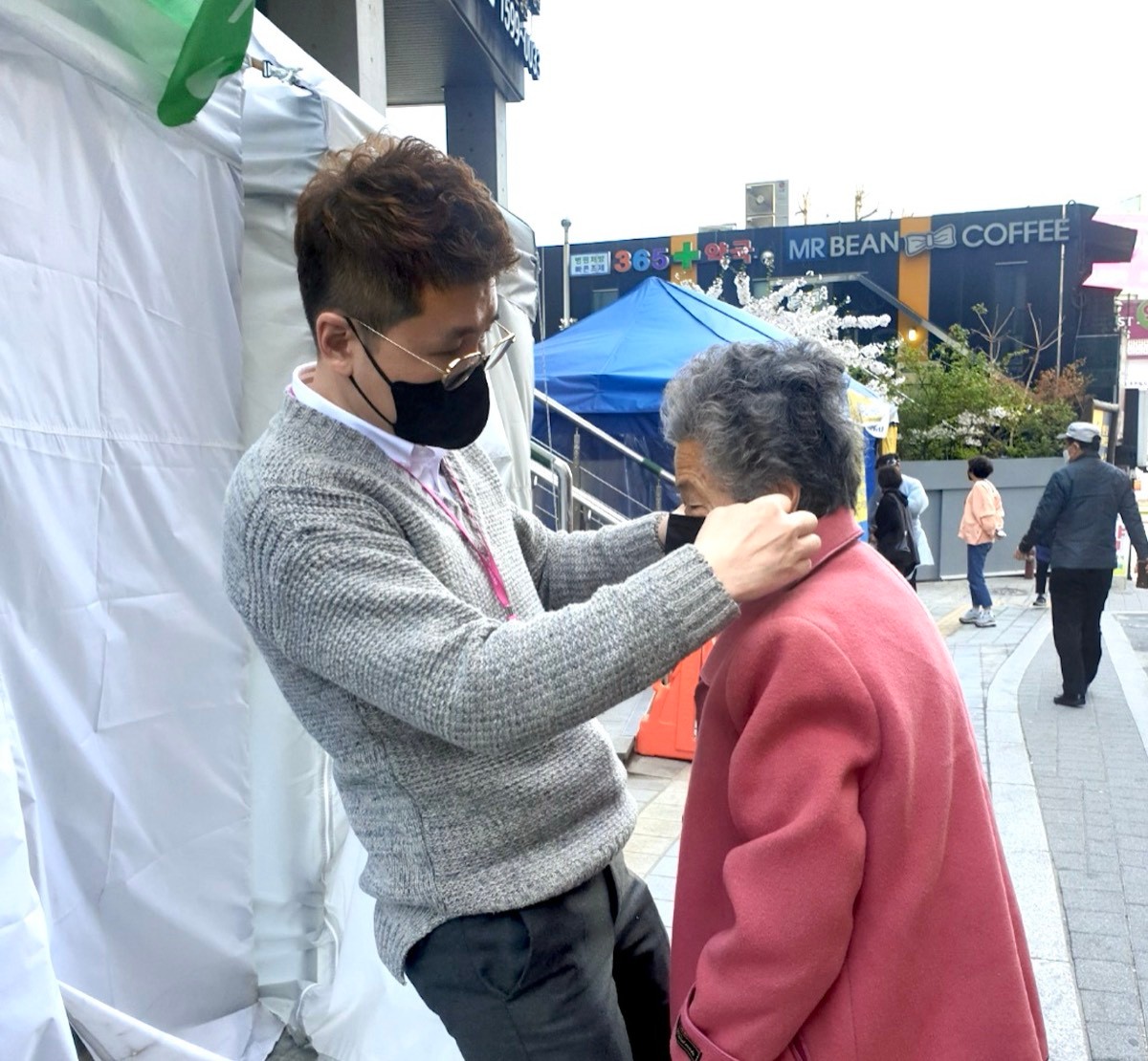 야외에서 남성이 어르신의 옷매무새를 매만지는 모습