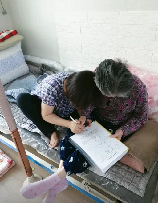어르신이 침대에서 혼자 글을 쓰는 모습