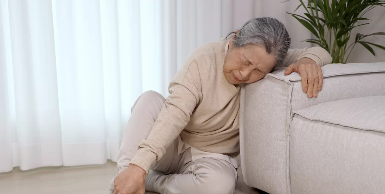 어르신이 소파 옆 바닥에 주저앉아 힘들어하는 모습