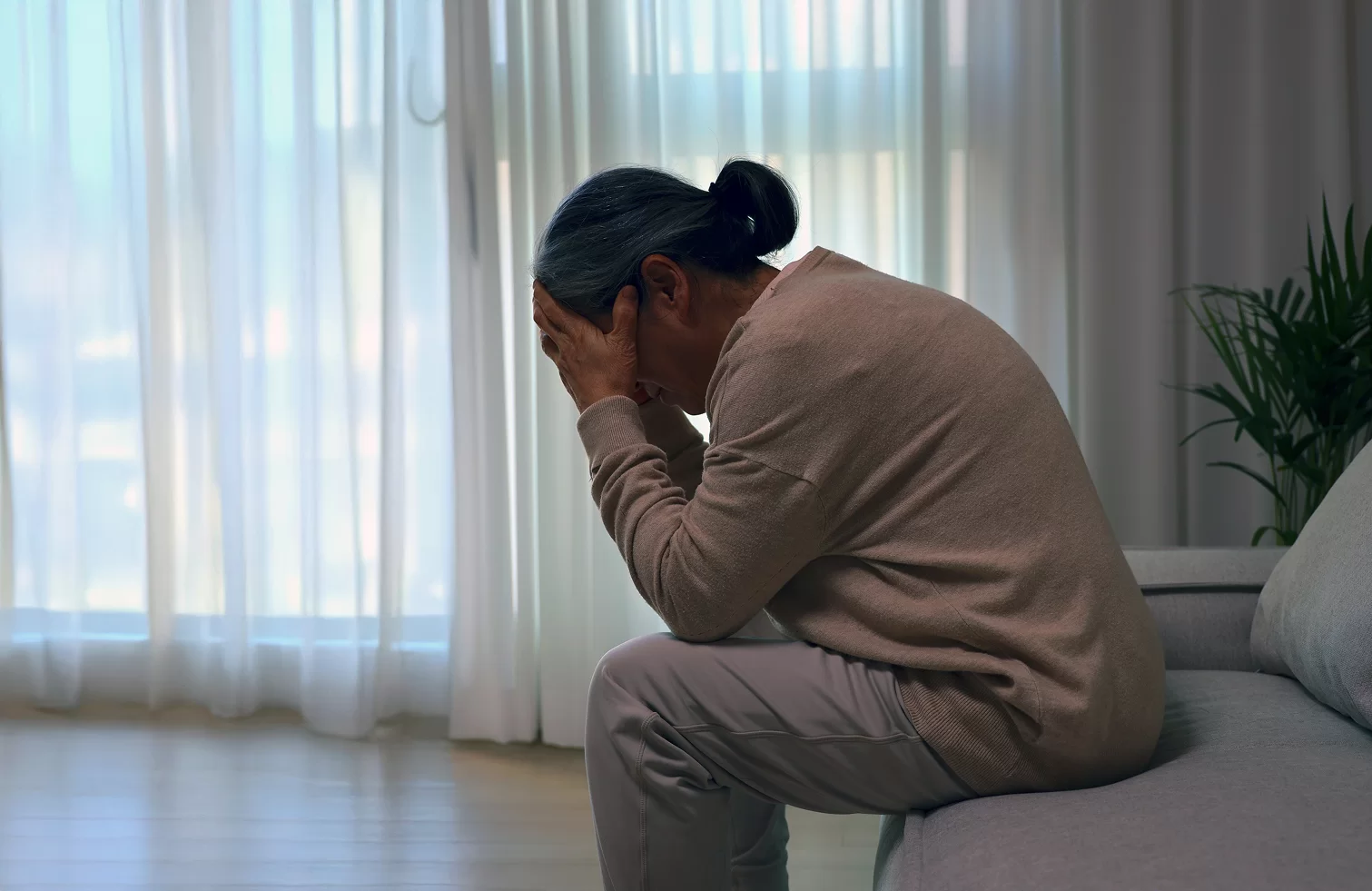 어르신이 침대에 앉아 손으로 얼굴을 감싼 모습